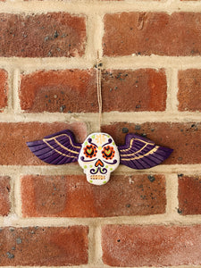 Hanging wooden skull with purple wings.